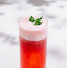 Red cocktail with foam and basil leaves on white background with shadows