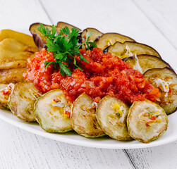 Delicious grilled vegetables with tomato sauce and herbs on white plate