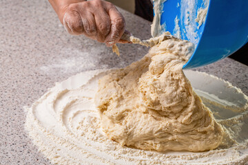 Healthy baking with sourdough starter. Woman kneading dough by hand yeast dough. Hand woman pours dough from a bowl onto the table. Pouring sourdough discard from a bowl directly on the table