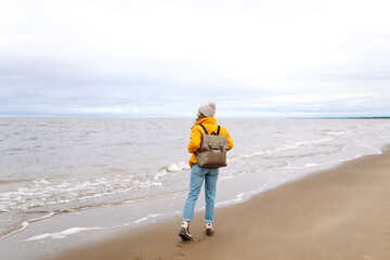 Young woman tourist walking beach on cloudy day. Autumn near the sea. Travel, tourism concept. Active lifestyle.
