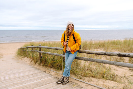 Young woman tourist walking beach on cloudy day. Autumn near the sea. Travel, tourism concept. Active lifestyle.