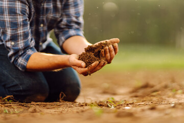 Close up of male hands touching soil on the field.  Farmer is checking soil quality before sowing....