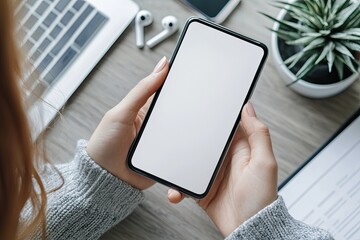 Mockup image of woman's hands holding smartphone with blank screen on gray table background, top view
