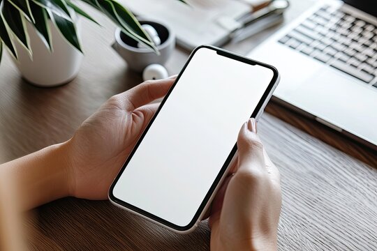 Mockup image of woman's hands holding smartphone with blank screen on gray table background, top view