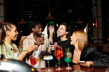 Colleagues joyfully raise colorful cocktails, enjoying the festive atmosphere together.