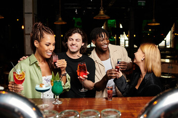 Excited coworkers toast with colorful cocktails while enjoying a joyful atmosphere together.