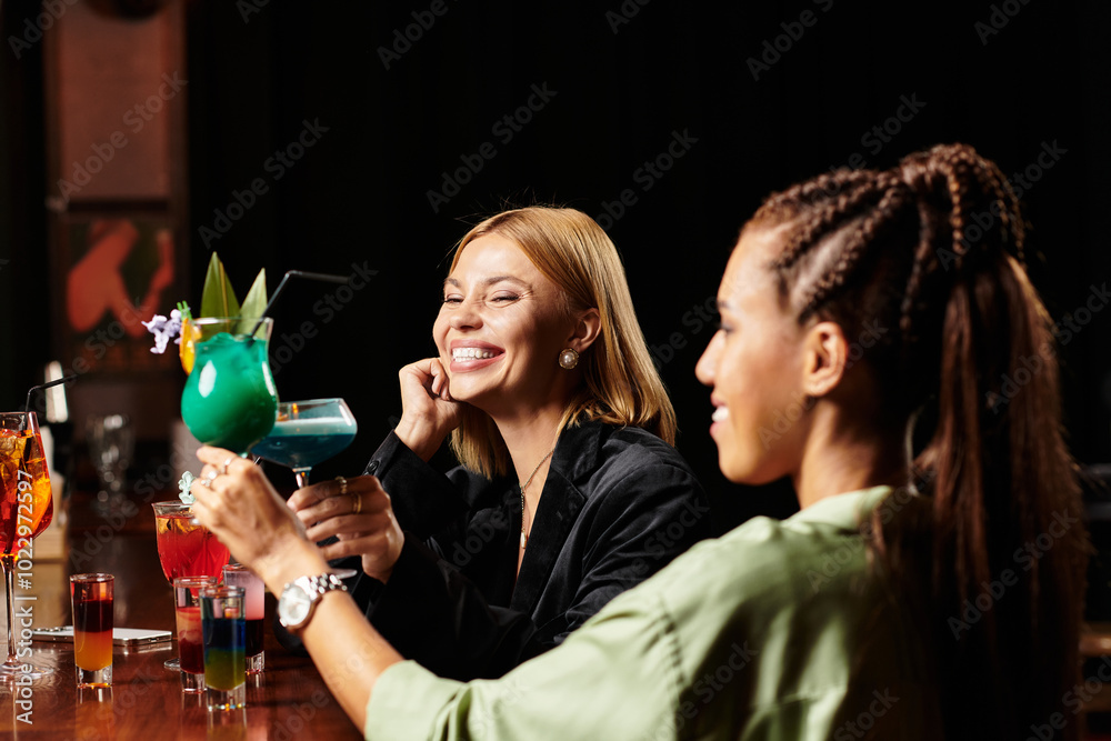 Wall mural two young professionals enjoy colorful cocktails and laughter during a corporate celebration.