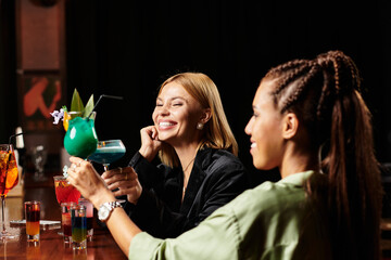 Two young professionals enjoy colorful cocktails and laughter during a corporate celebration.