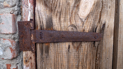 Rusty hinges of an old wooden door. An old brick building with an old two-door