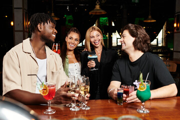 Colleagues toast with colorful cocktails while exchanging lively banter at a fun gathering.