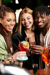 Colleagues share laughter and clink glasses in a lively atmosphere during a nighttime gathering.