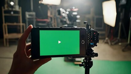 A smartphone displays a green screen while mounted on a tripod, indicating a video recording setup in a studio environment.