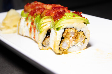 Close up of sushi roll with fried shrimp inside and fresh avocado and salmon on the top