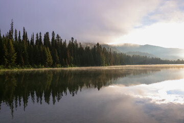 Fototapeta premium the steaming lightning lake in British Columbia in the early morning sunlight, while the forest is reflected in the calm water surface