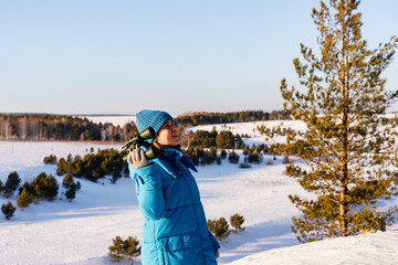 Smiling woman ecologist in blue jacket and hat with binoculars in hand looking up at bird migration...