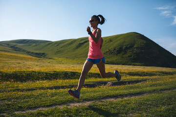 Fitness woman runner running at flowering grassland mountain top