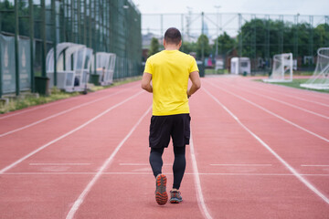 Fototapeta premium Backside view of a man in comfortable activewear run along the track stadium, active and healthy lifestyle on a contemporary sports arena in the town park. 