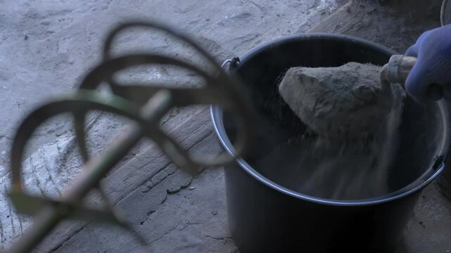 Dry wall putty mix is poured into black bucket for home repair. Later, it will be mixed with water to form paste that can be used to smooth walls. DIY home improvement in progress
