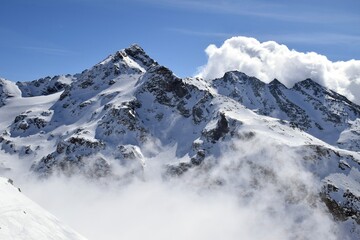 Obraz premium Snowcapped Alpine mountains peaking through clouds in the Three Valleys, France. Breathtaking view from ski resort in French Tarentaise Valley.