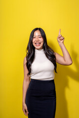 A woman is standing in front of a yellow wall, smiling and pointing her finger