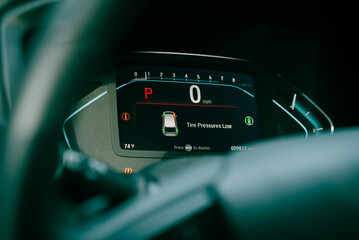 Close-up tire pressure low indicator displays on instrument panel of modern car minivan in Parking mode, tire pressure monitoring system TPMS indicates lights on driver information interface