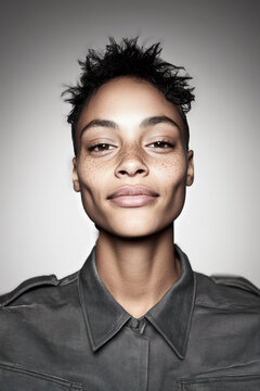 Confident young individual with a buzzed hairstyle and a warm smile, wearing a casual shirt, exuding friendliness, joy, and a spirited demeanor.