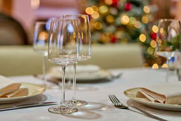 Christmas festive modern restaurant interior with greenery, pleasant cozy lighting and festive table setting with glasses.