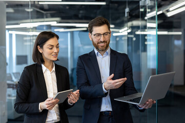Two business professionals engaging in project discussion in modern office setting. Woman holding a...
