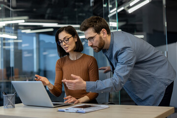 Colleagues collaborate in modern office environment, focusing on laptop screen for work-related discussion. Engaged teamwork fosters creativity, productivity, innovation in professional setting.
