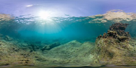 A rocky underwater environment captured in a 360-degree panorama, with sunlight penetrating through the water. The peaceful marine scene highlights coral and natural formations along the ocean floor.