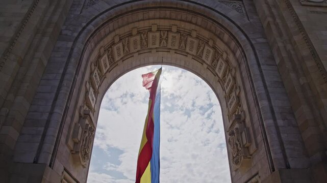The Romanian flag waving in the wind at the triumphal arch. The Red, Yellow and Blue tricolor. The wind that flutters and moves the flag hanging from the monument of the triumphal arch in Bucharest.