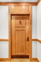 A front door detail with a wooden door, black knocker and doorknob, and wood trim on white walls.
