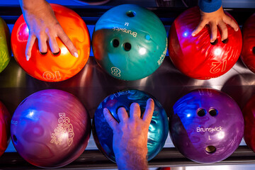 Photo with bowling balls in different colors and a person's hand reaching for them for a fun night...