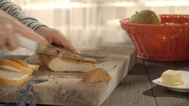 A woman trying to cut a french bun with a dull knife in the kitchen. 