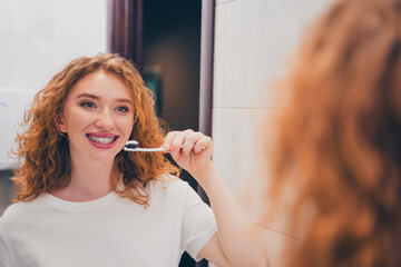 Photo of adorable woman brushing teeth with toothbrush in bathroom interior in the morning indoors