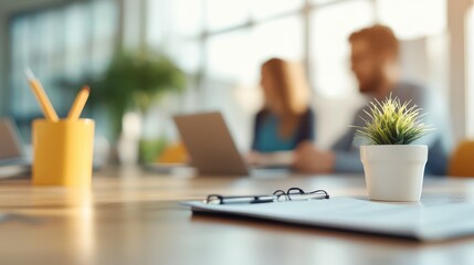 A small green plant decorates a table where two colleagues engage in conversation while using laptops, demonstrating a collaborative and vibrant office setting.