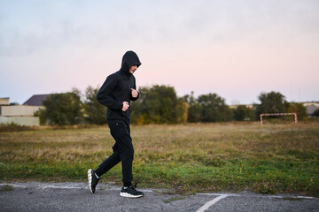 Young guy jogging early in the morning in the park in black sportswear