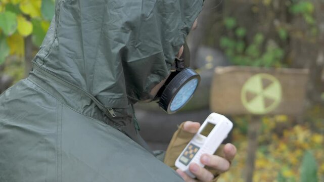 Man in protective suit with dosimeter inspects radioactive zone. Radioactive pollution. Radiation symbol, yellow ionizing warning sign background