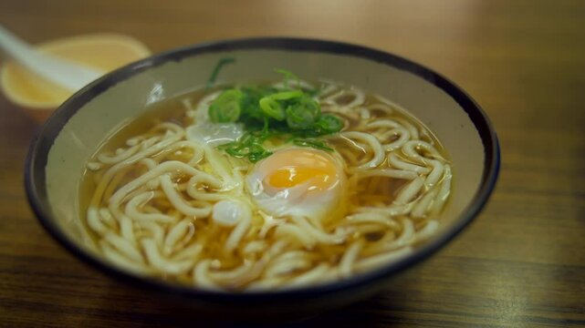 Close up of a steaming hot tsukimi udon with egg and spring onion garnish