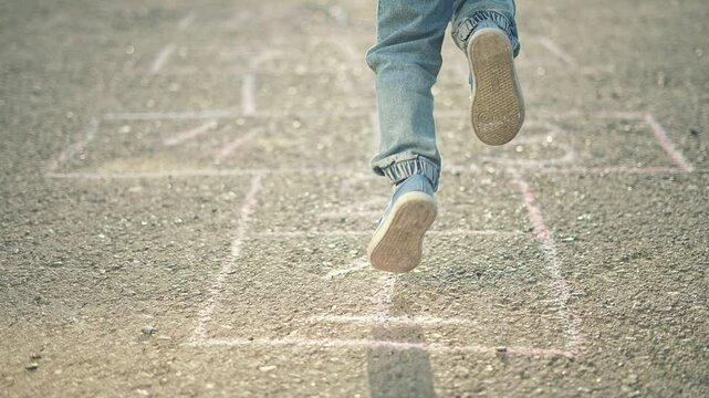 Kid playing hopscotch outdoors. Close up foot hopping chalk squares during hopscotch game. Joyful kid hop in sunlight. Fun childhood hopscotch game. Kid enjoys outdoor activity hopping hopscotch game.