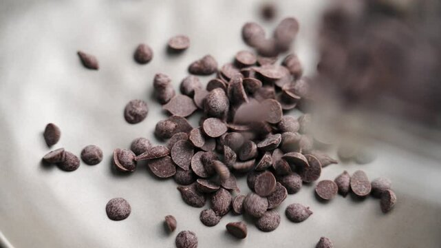 Organic dark chocolate chips or drops falling into a kitchen bowl in slow motion for preparing baking ingredients. Top view