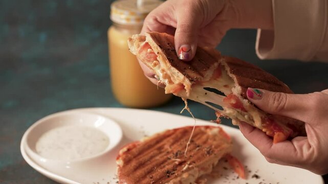 close up view of woman's hands breaking a delicious vegetarian toasted sandwich with melted cheese