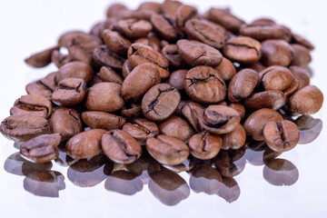 Close up of coffee beans on a reflective mirror surface with a white background, highlighting the texture and detail of roasted coffee beans