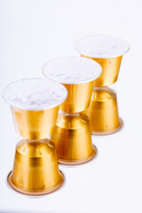 Golden Coffee Capsules Reflected on a White Mirror.A stunning close-up of three golden coffee capsules resting on a white mirror