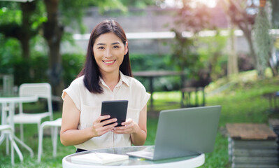 Asian business woman working outside freelancer using computer laptop and digital tablet device wireless remote communication technology, online worker casually enjoying outdoor in nature sunlight.