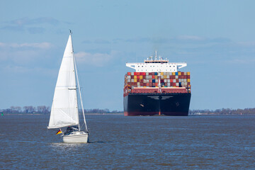A sailboat in front of a huge container ship on Elbe river
