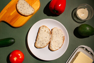 Two slices of bread with butter on the white plate. Flat lay of the breakfast preparation on dark green background. Traditional breakfast concept. Top view
