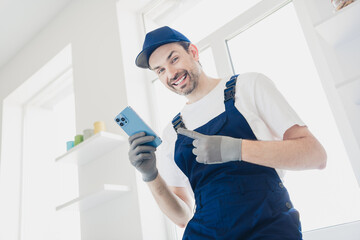 Smiling handyman in overalls using smartphone during home renovation project in bright modern room