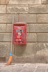 Broom leaning on red postbox at wall in Italy