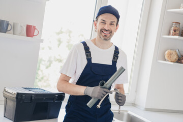 Smiling young handyman holding plumbing tools in a modern kitchen, ready for a repair job